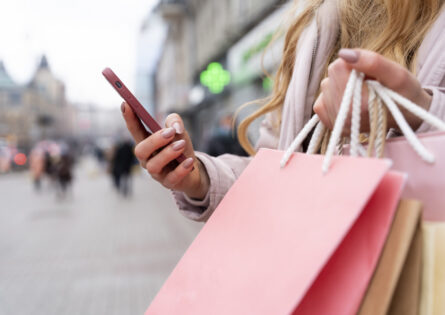 Une personne tient ses sacs suite à de nombreux achat et consulte son smartphone